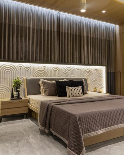 Bedroom with arched fluted panel wall, backlit cove lighting, layered taupe bedding and floor-length curtains
