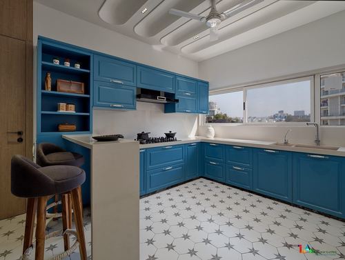 Teal blue L-shaped kitchen with star-patterned floor tile, open shelving and city view through windows