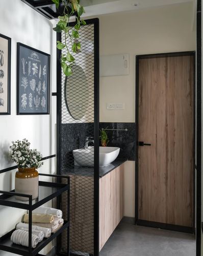 Bathroom vanity behind black mesh partition with oval mirror, stone counter, and wooden door