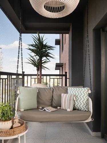 Cane hanging swing with cushions on a balcony overlooking city buildings