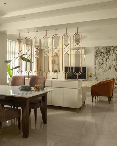 Dining area with brass oval-link partition, wood table, and glossy cream sideboard leading to living room