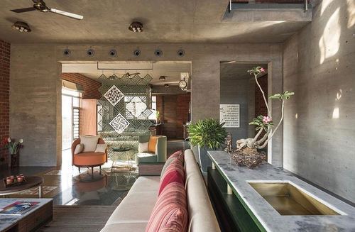 Living room with exposed concrete walls, jali screen partition, orange armchairs and marble-brass console