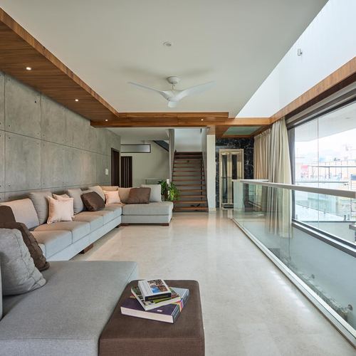 Living room with grey sectional sofa, concrete wall, timber ceiling beam and glass balcony railing
