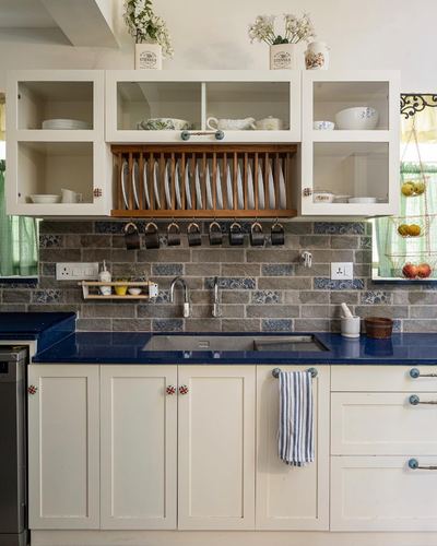 White kitchen with navy countertop, patterned tile backsplash, and a wooden plate rack under glass cabinets