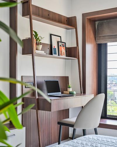 Wall-mounted wood desk with laptop below leaning ladder shelving near a window