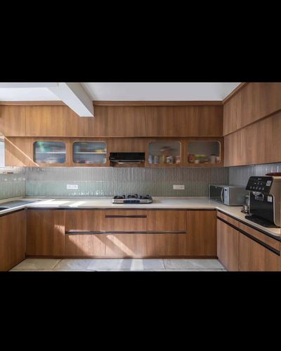 U-shaped wooden kitchen with gas hob, glass cabinets, ribbed grey backsplash and sunlight streaming across counter