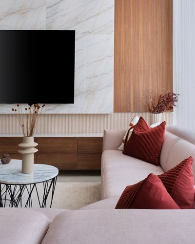 Living room corner with marble feature wall, wood panel, blush sofa and red velvet cushions