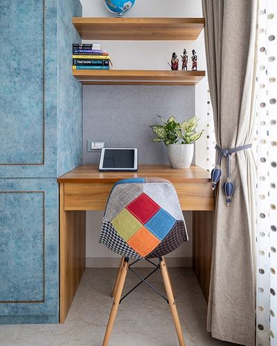 Study nook with wooden desk, floating shelves, blue textured wardrobe and patchwork chair