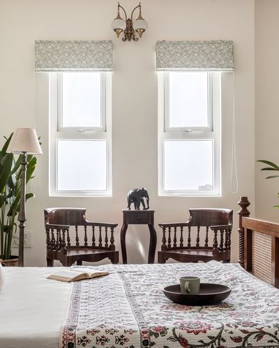 Bedroom with twin windows, carved wood chairs, elephant figurine and floral bedspread