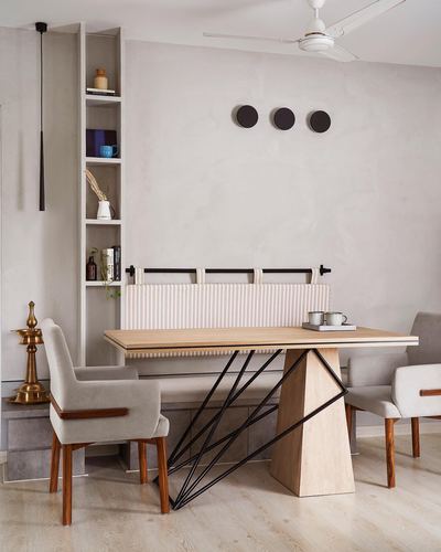 Neutral dining room with wooden table on angular black metal base, striped bench, and vertical shelving niche