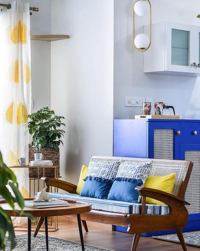 Living room corner with cane-backed wooden settee, blue patterned cushions, and blue cabinet with cane doors