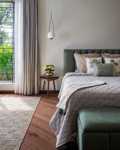 Bedroom with green tufted headboard, wooden side table, pendant light, and window framing greenery
