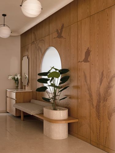 Foyer with oval mirror, wood-panelled wall with bird motifs, bench, and potted plant