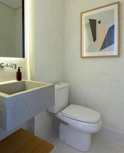 Minimalist powder room with sculpted stone sink, backlit mirror, and framed abstract art above toilet