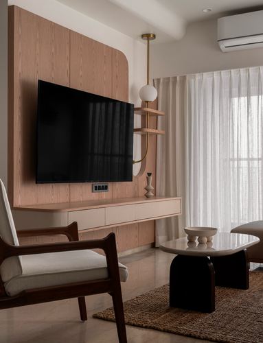Living room with curved wood tv panel, brass pendant light, marble coffee table and cane armchair