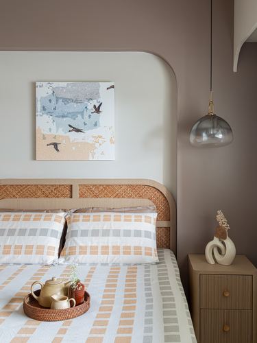 Bedroom with arched cane headboard, checkered bedding, smoky glass pendant, and bird artwork above.