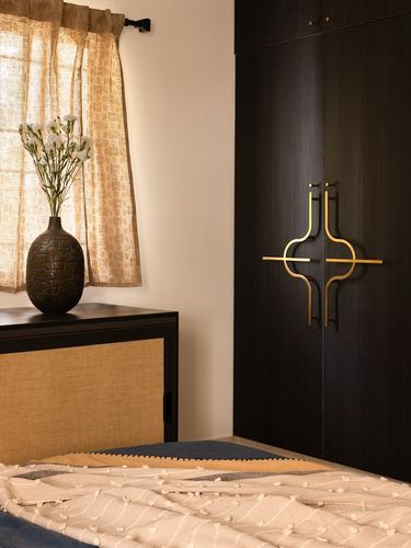 Bedroom corner with dark wardrobe, brass sculptural handles, cane cabinet and vase of flowers