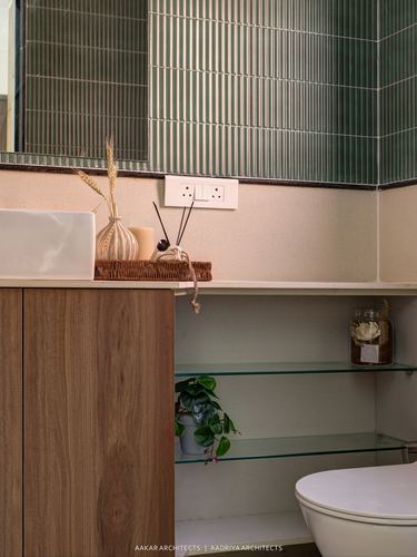 Bathroom vanity corner with wood cabinet, ribbed green tile wall, and glass shelves