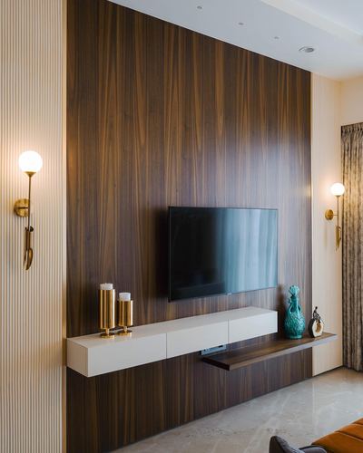 Wood-panelled TV wall with brass sconces and a floating white console below