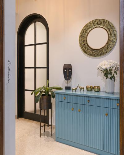 Foyer with teal fluted console, round mirror, mask sculpture and arched glass door