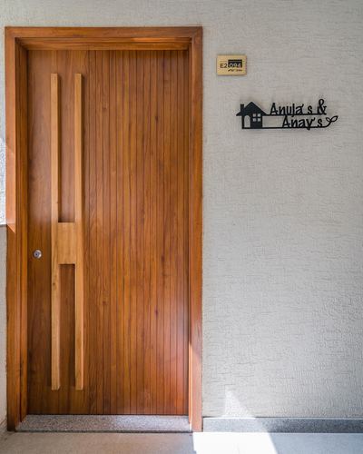 Wooden entrance door with vertical carved pulls beside textured wall and nameplate