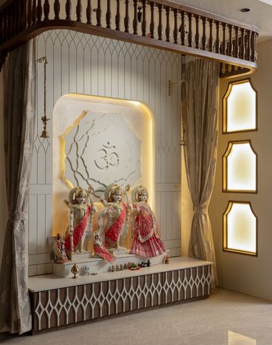 Pooja room with three idols in arched niche below carved balustrade, backlit amber glass panels beside