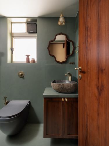 Sage green bathroom with stone vessel sink, wooden vanity, and scalloped mirror beside a wooden door