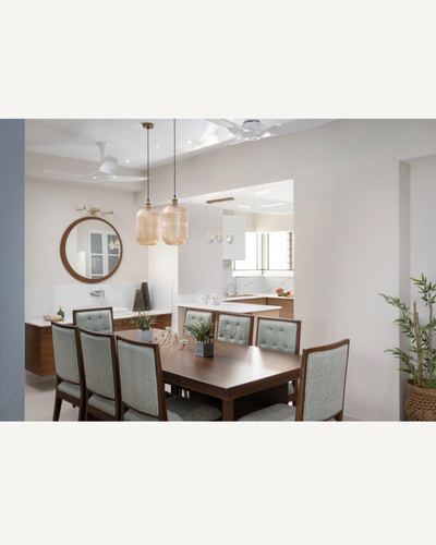 Dining room with wooden table, sage tufted chairs, round mirror, and glass pendant lights
