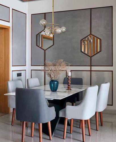 Dining room with marble table, grey upholstered chairs, wall paneling and hexagonal mirrors under a brass chandelier