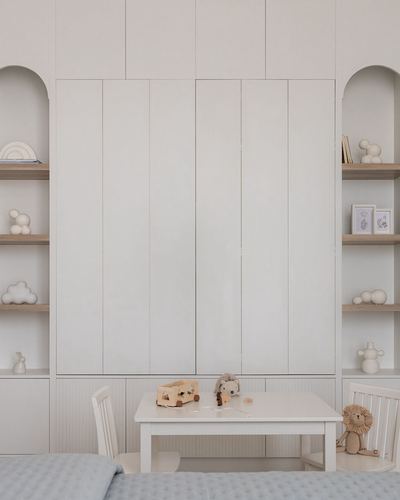 Child's bedroom with fluted wardrobe wall flanked by arched shelves and a small white play table