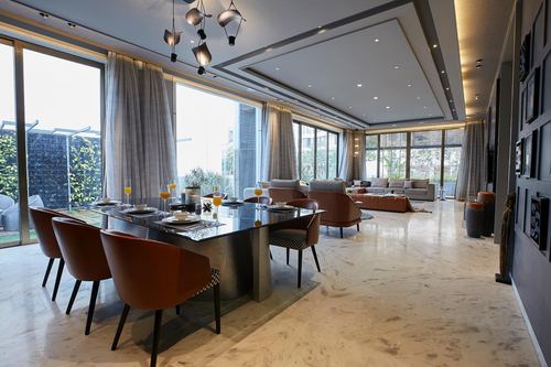 Open plan living-dining space with stone floors, rust leather chairs, glass dining table and floor-to-ceiling windows