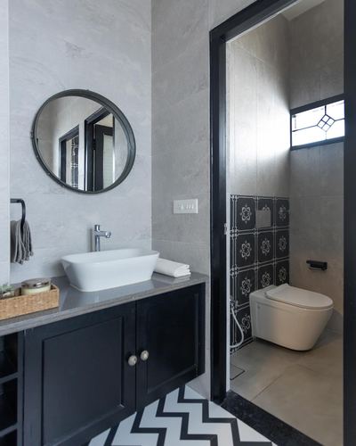 Bathroom with round mirror, black vanity, chevron floor and view into toilet with patterned tile wall