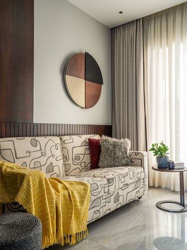 Living room corner with patterned sofa, mustard throw, round wood wall art and sheer curtains