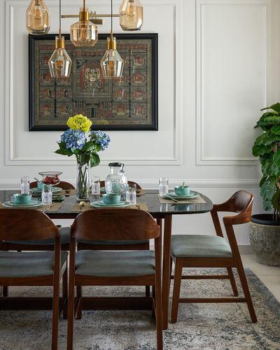 Dining room with marble table, wood chairs, amber pendant lights, and framed tapestry on paneled wall