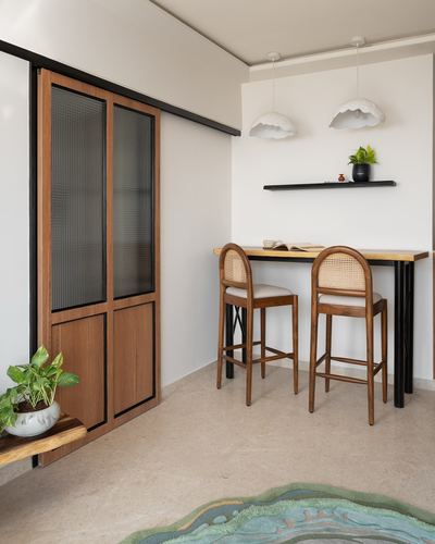 Small dining nook with cane-backed stools, high table, cloud pendant lights, and reeded-glass sliding door
