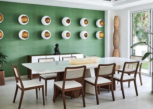Dining room with green textured wall, white ceramic wall sculptures, and cane-back wood chairs around a white table