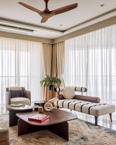 Sunlit living room with sheer curtains, wooden ceiling fan, and layered coffee tables