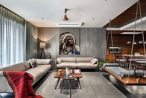 Grey-toned living room with beige sofas, tribal portrait art, and a hanging wooden swing near the dining area
