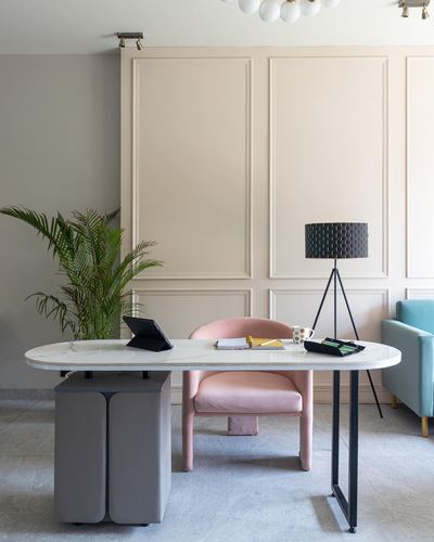Home office with oval stone-top desk, pink velvet chair, and tripod lamp against paneled wall