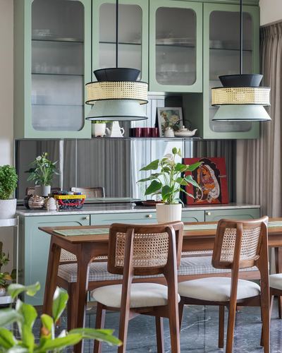 Sage green kitchen with cane pendant lights over a wooden dining table with cane-back chairs