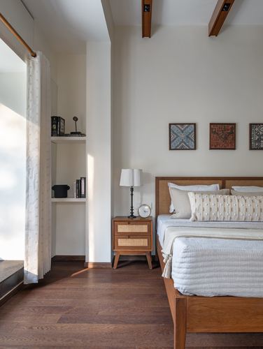 Bedroom with cane headboard bed, wooden floor, and framed textile art beside sunlit alcove