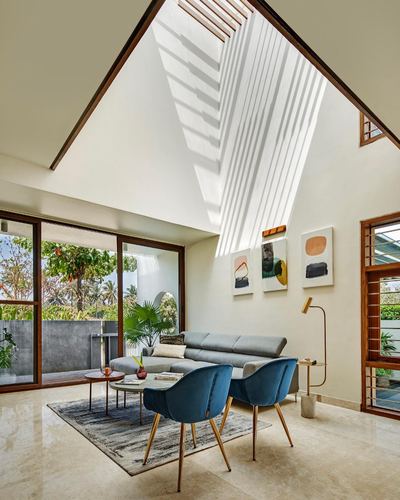 Living room with grey sectional, blue velvet chairs, and dramatic skylight casting striped light