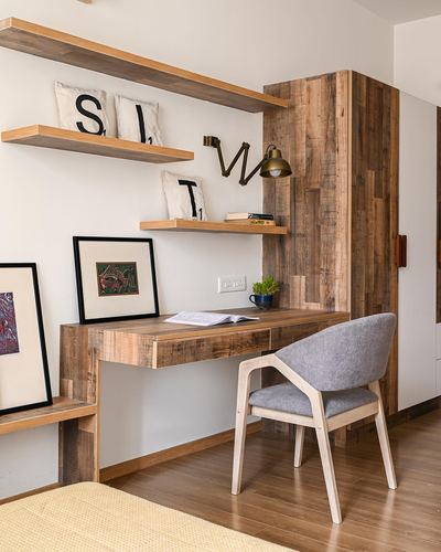 Wood-clad study nook with floating shelves, brass sconce, desk and grey upholstered chair