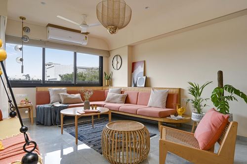 Pink banquette sofa with cane accents beneath window, rattan stool and coffee table in bright living room