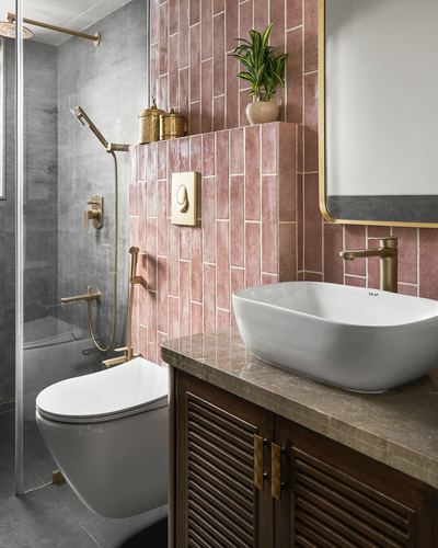 Bathroom with pink vertical tile, grey shower area, brass fixtures, vessel sink on stone counter over wood cabinet