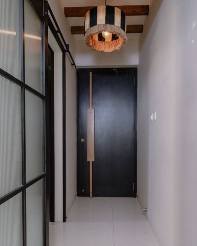 Narrow foyer with black door, fringed pendant light, and fluted glass partition