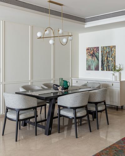Dining room with black wood table, grey curved chairs, brass chandelier, and paneled walls
