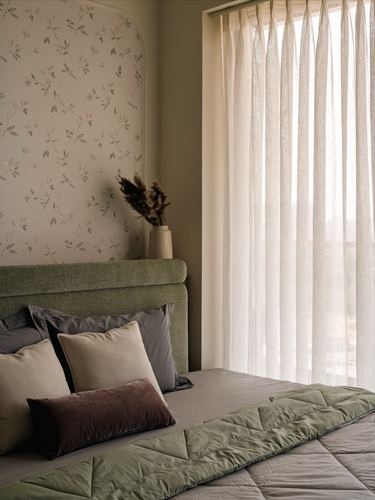 Bedroom corner with green upholstered headboard, floral arched wallpaper niche, and sheer curtains lit by daylight