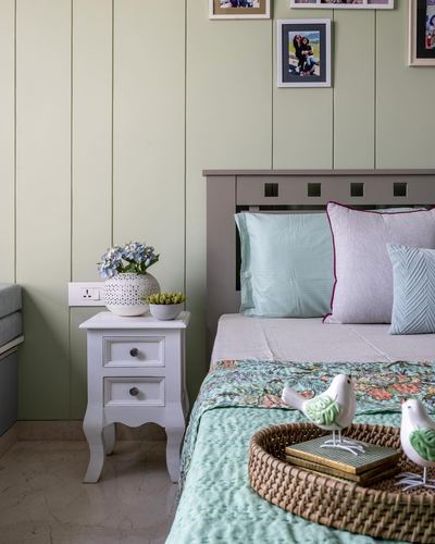 Bedroom corner with green paneled wall, upholstered bed and white bedside table with vase