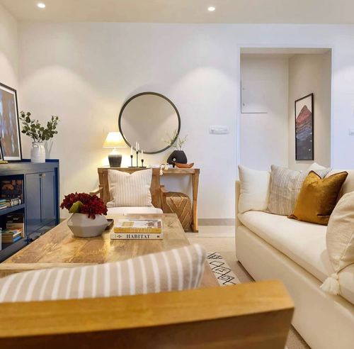 Cream sofa with mustard velvet pillow beside a wooden console and round mirror in a living room
